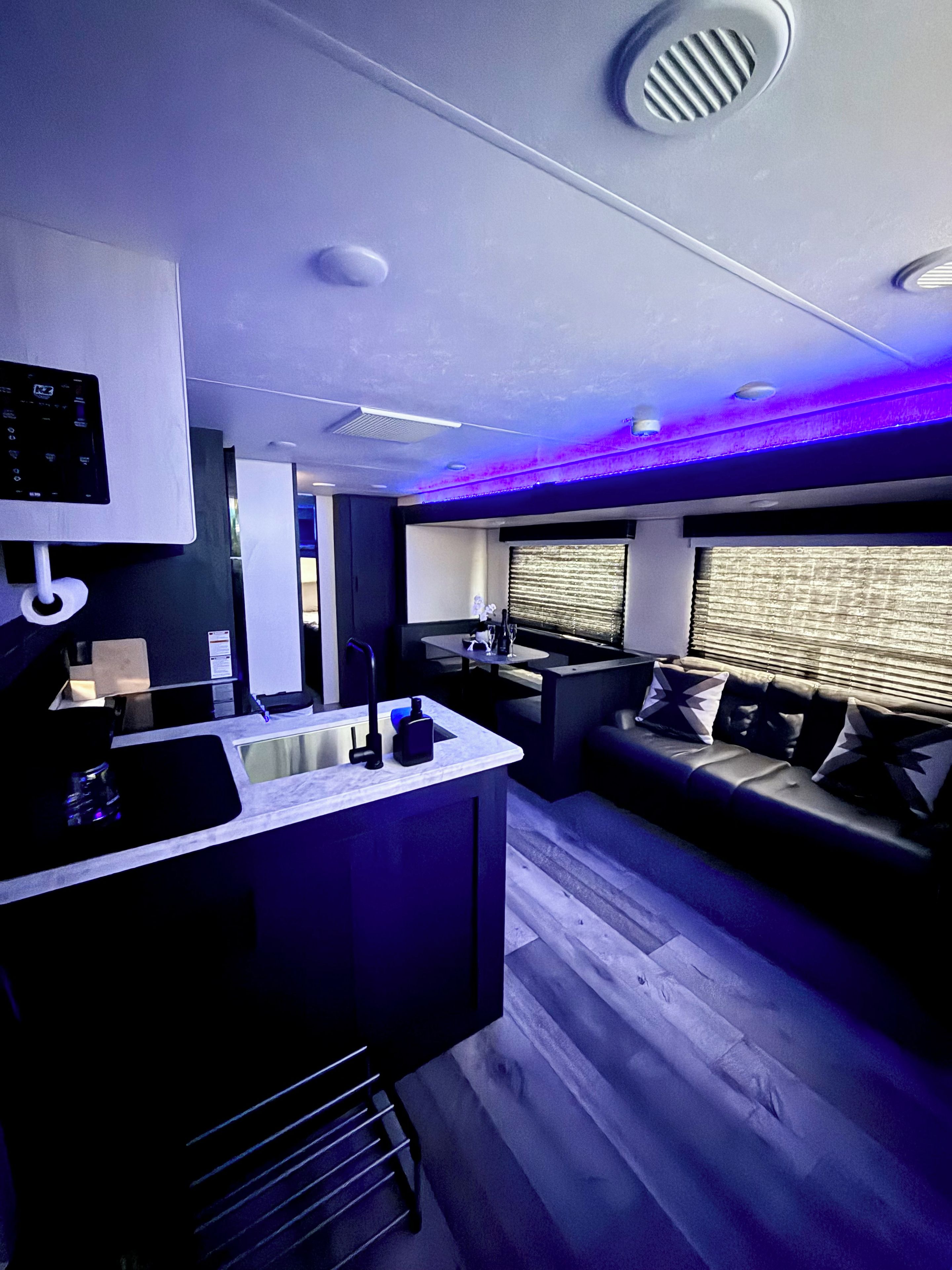 A modern kitchen with a built-in island, a seating area with a sofa and a window with blinds, and a ceiling with recessed lighting.