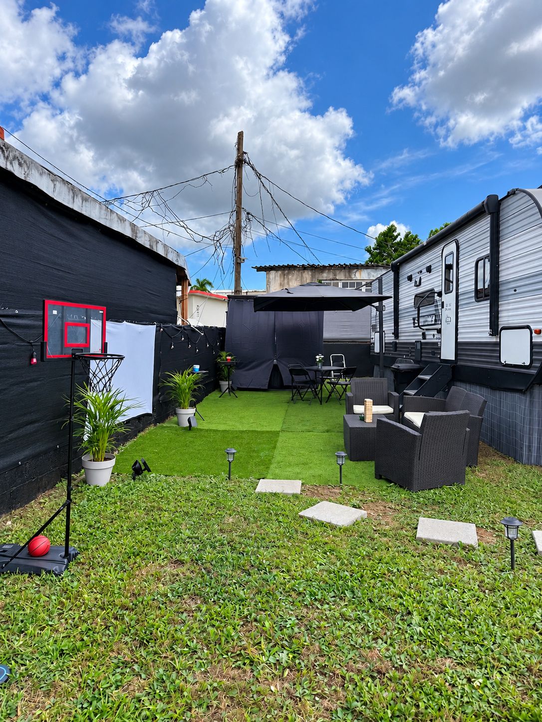 Un patio trasero con césped artificial, aro de baloncesto, mobiliario exterior y una caravana.