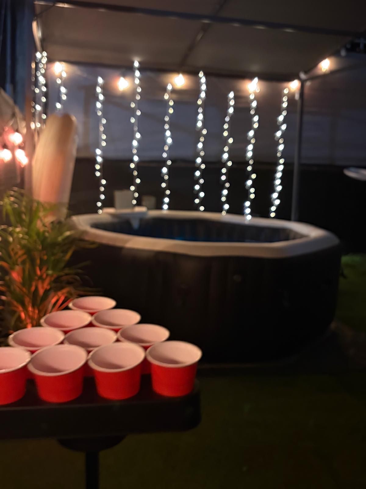 Un bain à remous avec une table devant, sur laquelle sont disposées des gobelets rouges, le tout éclairé par des guirlandes lumineuses.