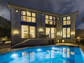 Ein modernes, zweistöckiges Haus mit Swimmingpool, großen Fenstern und Sitzgelegenheiten im Freien.