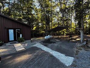 A rustic cabin with a metal roof and a well-maintained gravel driveway leading to a covered outdoor area. - Empty Nest, your place to land when you're away from home. (Columbia)