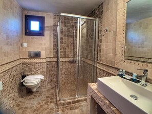 A bathroom with a glass shower enclosure, a toilet, and a sink with a mirror. - Hotel Apsis (Emporio)