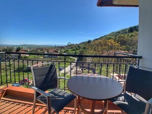 A balcony with a table and chairs, overlooking a hilly landscape with houses. - Hotel Apsis (Emporio)