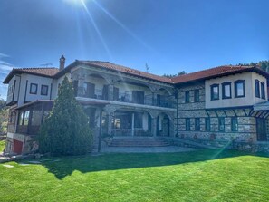 A large, two-story house with a covered porch and a well-maintained lawn. - Hotel Apsis (Emporio)