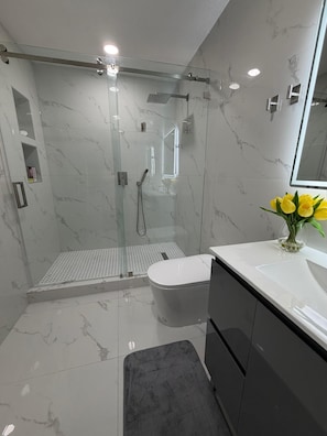Un bany modern amb dutxa de vidre, vàter i un lavabo amb un ram de flors grogues.