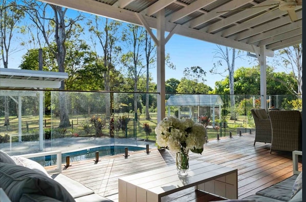 Covered poolside deck area enclosed by glass fencing and furnished with comfortable outdoor lounge seating.    - The Oak Estate | Acreage Retreat with Pool (Nerang)
