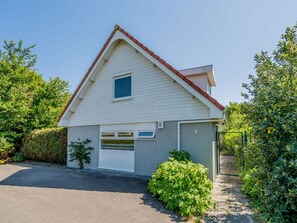 A single-story house with a gabled roof, a garage, and a small front yard with a hedge. - Holiday Apartment With 2 Bedrooms (Renesse)