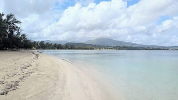 Una playa con agua cristalina, una orilla arenosa y una cadena montañosa distante.
