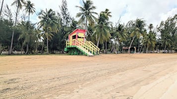 Una playa arenosa con una escalera colorida que lleva a una estructura de techo rojo.