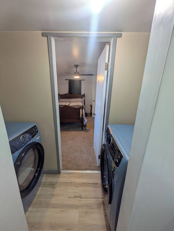 A laundry room with two washing machines, a bed in the background, and a ceiling fan.