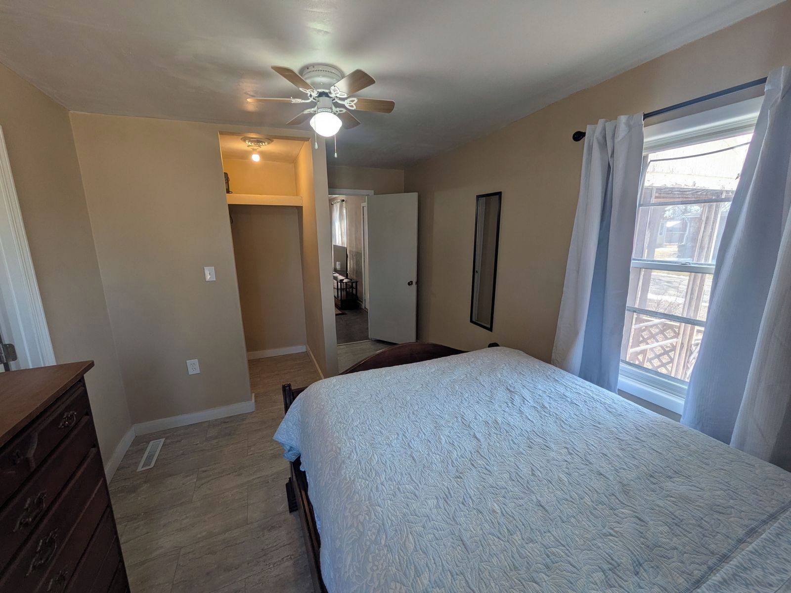 A bedroom with a bed, a ceiling fan, a window with curtains, and a door leading to a bathroom.