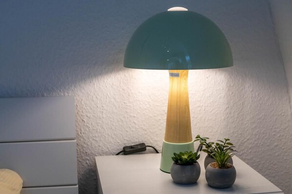 A lamp with a wooden base and a green dome shade, placed on a white table with two small potted plants beside it. - Dünenperle Vacation Rental (Norden)