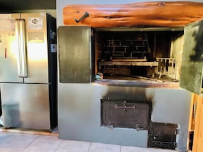 Eine Küche mit eingebautem Holzofen, einem Edelstahl-Kühlschrank und einem kleinen Stauraumschrank.