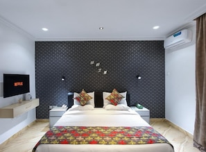 Una habitación de hotel moderna con una cama grande, un televisor de pantalla plana, un aire acondicionado de pared y una pared con estampado geométrico.