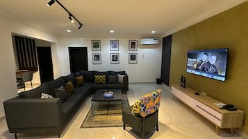 A modern living room with a sectional sofa, a coffee table, a colorful armchair, a flat-screen TV, and framed pictures on the wall.