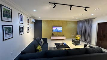 Una sala de estar moderna con un sofá negro grande, una mesa de centro, un televisor montado en la pared y cuadros enmarcados.