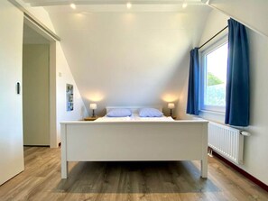 A bedroom with a bed centered under a sloped ceiling, a window with curtains, and a radiator on the wall. - Holiday Home With 2 Bedrooms (Oostkapelle)