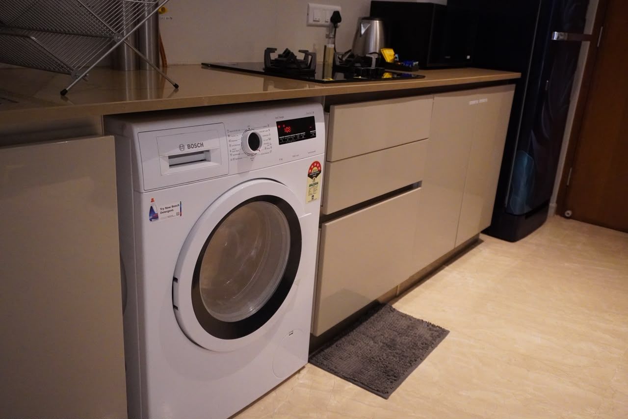 A compact kitchen with a Bosch washing machine, a coffee maker, and a microwave.