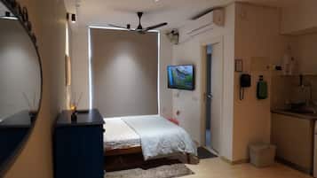 A bedroom with a bed, a ceiling fan, a TV, and a kitchenette.