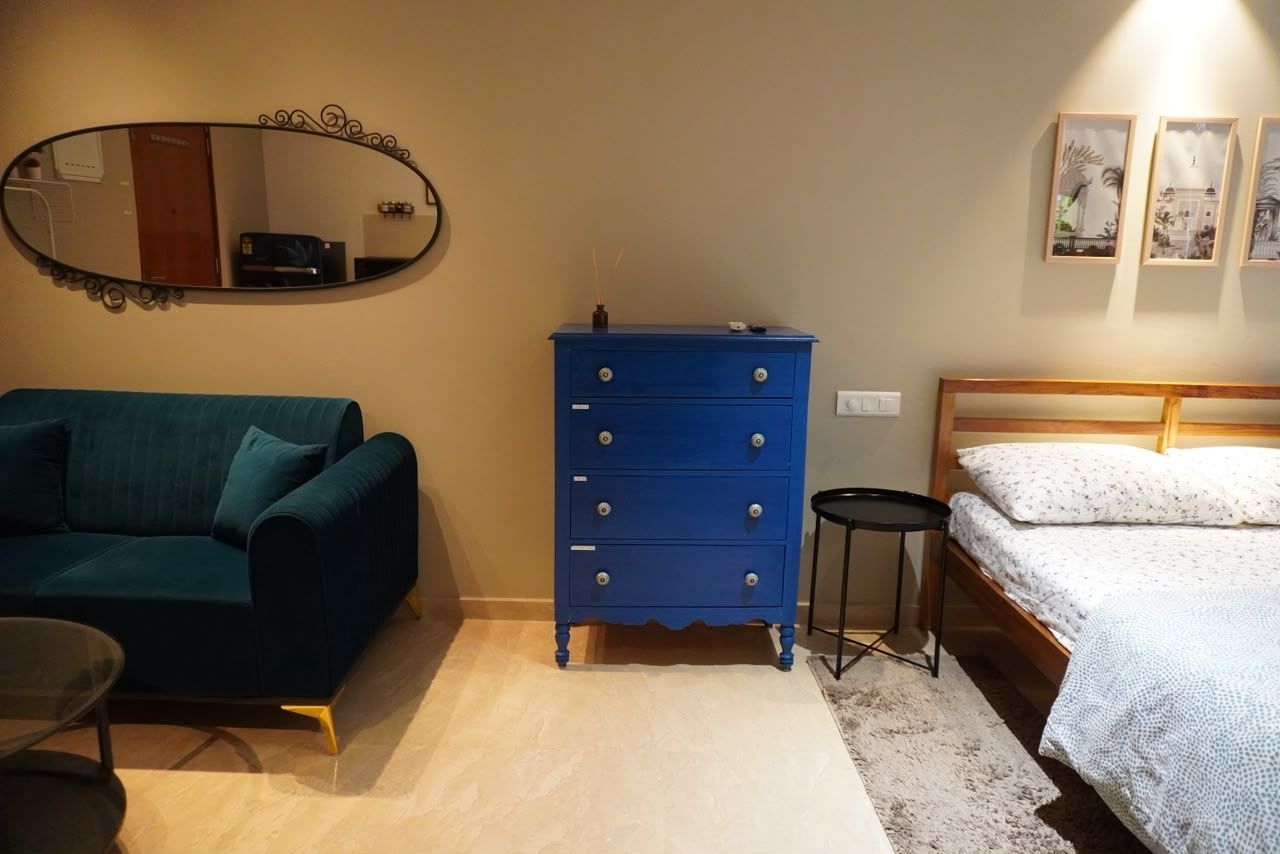A bedroom with a blue dresser, a bed, a mirror, and a small table.