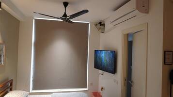 A bedroom with a bed, a ceiling fan, a mounted TV, and an air conditioning unit.