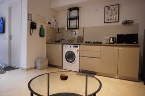 Een kleine keuken met een wasmachine, magnetron en een glazen tafeltje.