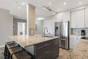 A modern kitchen with granite countertops, stainless steel appliances, and a central island with bar stools. - Gulf-View 2BR Condo | TOPS’L Resort & Beach Access (Miramar Beach)