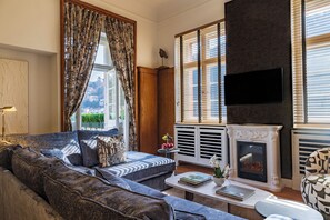 A living room with a fireplace, a sofa, a coffee table, and a television. - Signature Residences - River View (Heidelberg)