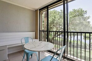 A balcony with a white table and two blue chairs, overlooking a body of water and trees. - Midnight Cove II – Unit 823- Bayside Classic (Sarasota)