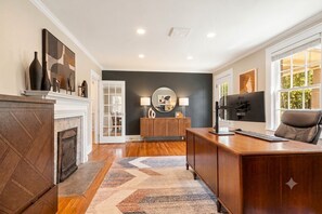A modern living room with a fireplace, a wooden desk, and a comfortable seating area. - Owens Retreat - Private Home on 2 Acres (Greer)