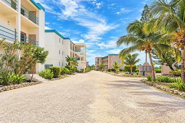 A multi-story hotel with a gravel driveway, palm trees, and a clear blue sky. - Sea View Ground-Floor Condo at Mara Laguna (San Pedro)