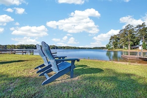 A lakeside view with Adirondack chairs, a dock, and a small building. - Lakefront Oasis - Dock, Pavilion & Kayaks (Prosperity)