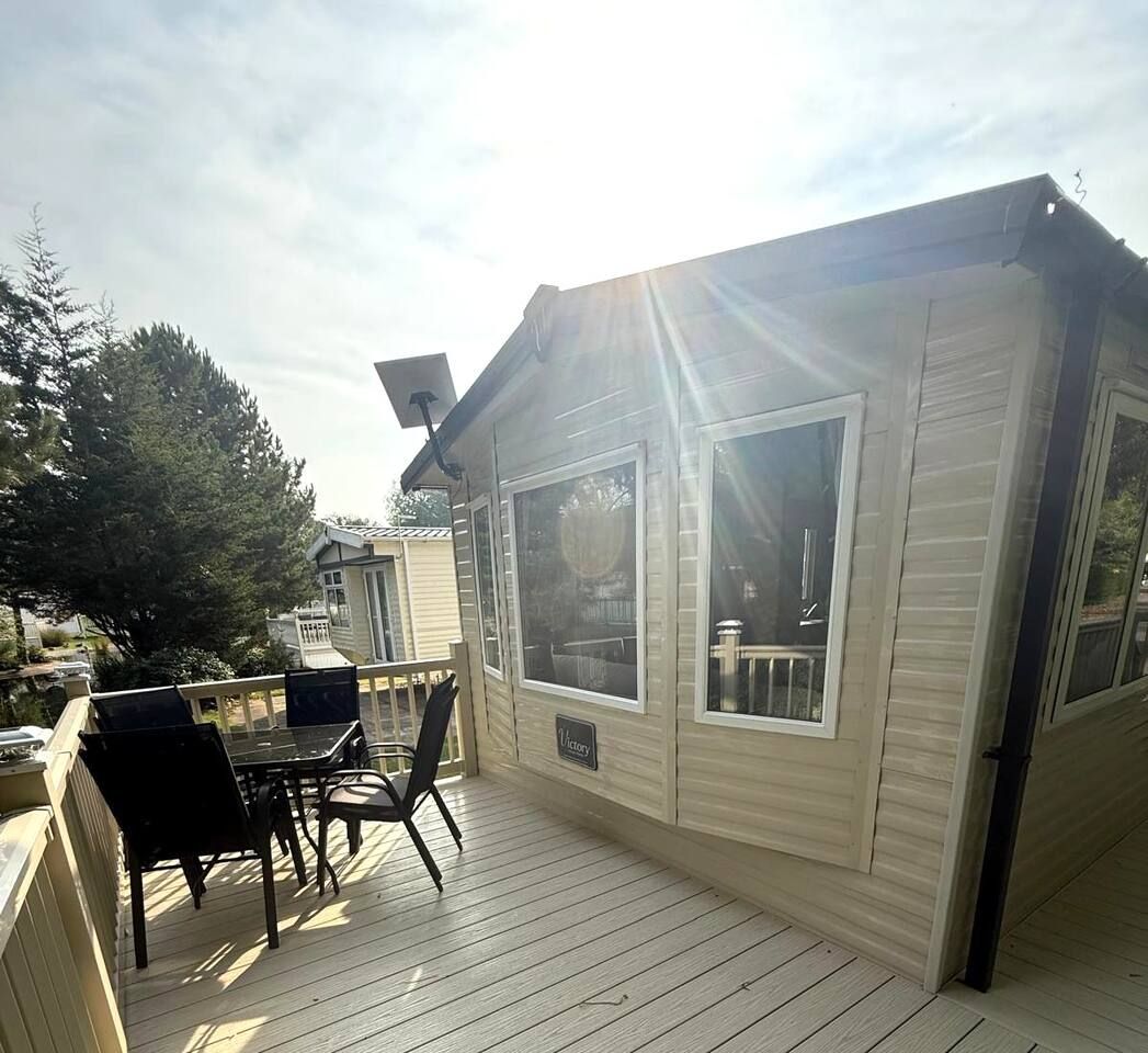 A wooden deck with a table and chairs, a covered area with a roof, and a view of the surrounding trees.