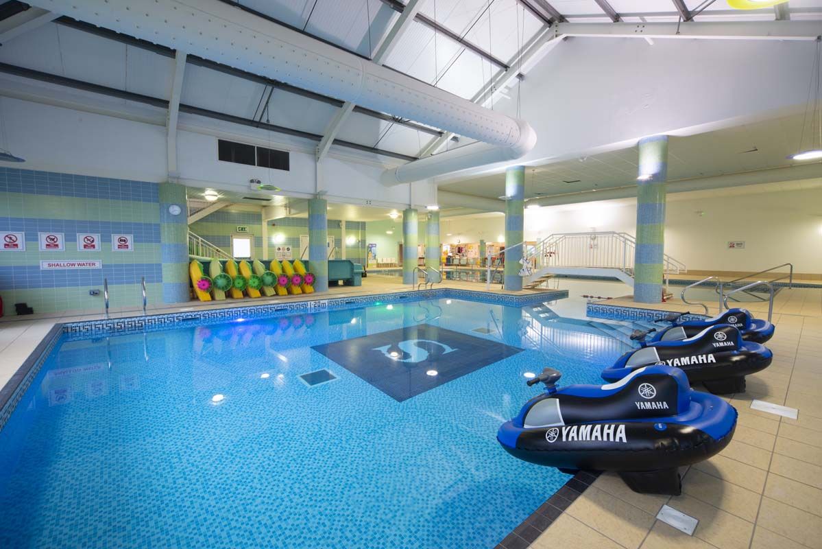 An indoor swimming pool with Yamaha watercraft, tiled walls, and a clear water sign.