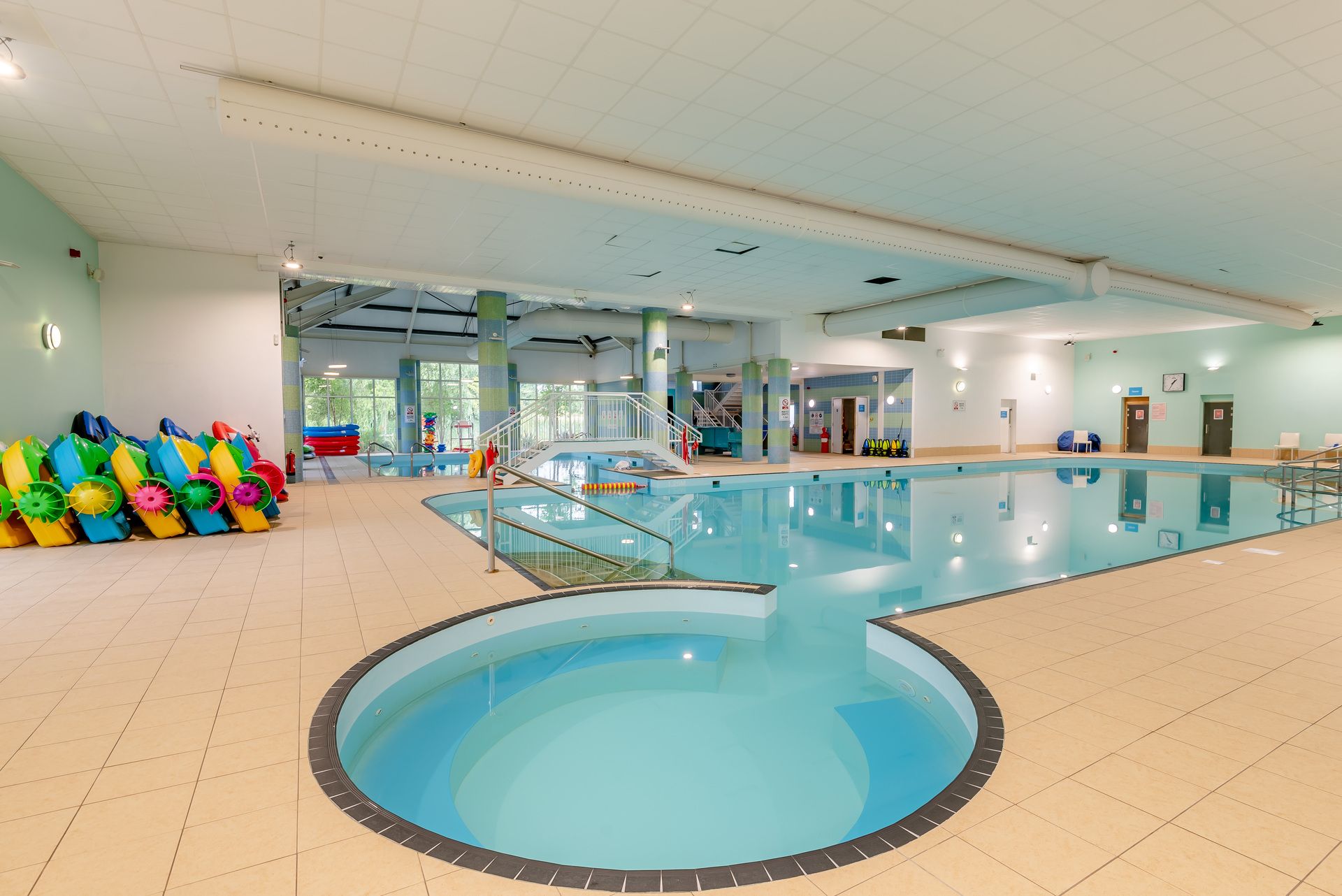 An indoor swimming pool with a central diving area, surrounded by tiled walls and a ceiling with grid-like patterns.
