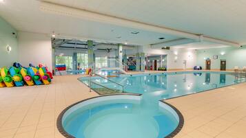 An indoor swimming pool with a central diving area, surrounded by tiled walls and a ceiling with grid-like patterns.