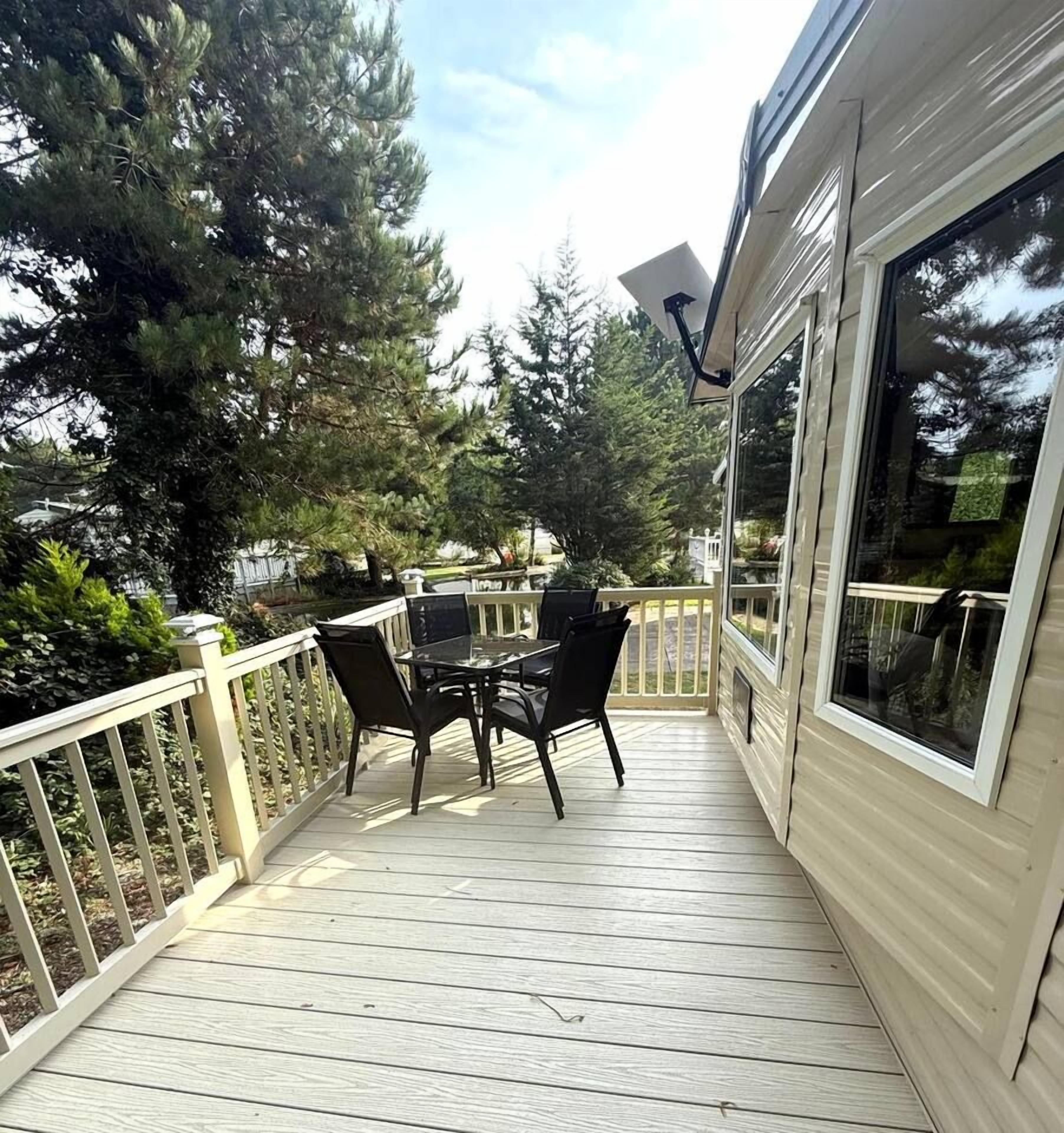 A wooden deck with a table and chairs, surrounded by a white railing and trees.