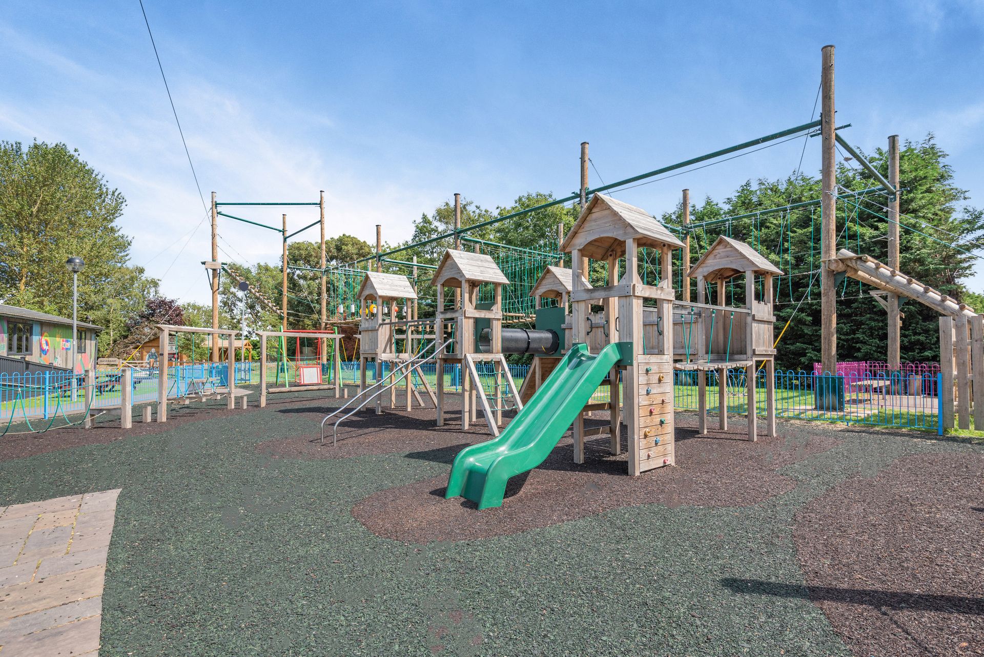 A playground with a green slide, climbing structures, and a fenced area.