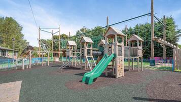 A playground with a green slide, climbing structures, and a fenced area.