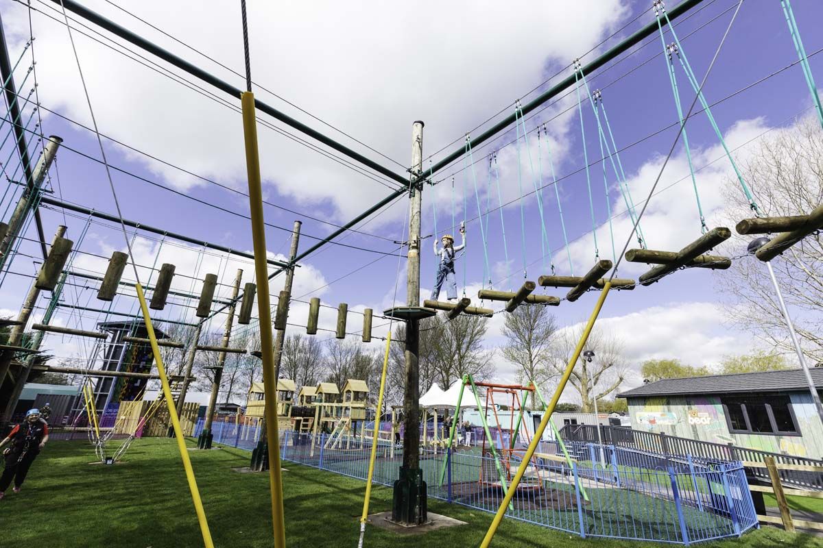 An outdoor adventure course with ropes, poles, and a fenced area.