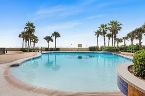 A swimming pool with a tiled edge, surrounded by palm trees and a clear sky. - Gulf Views • Beach Access • Indoor/Outdoor Pools (Orange Beach)