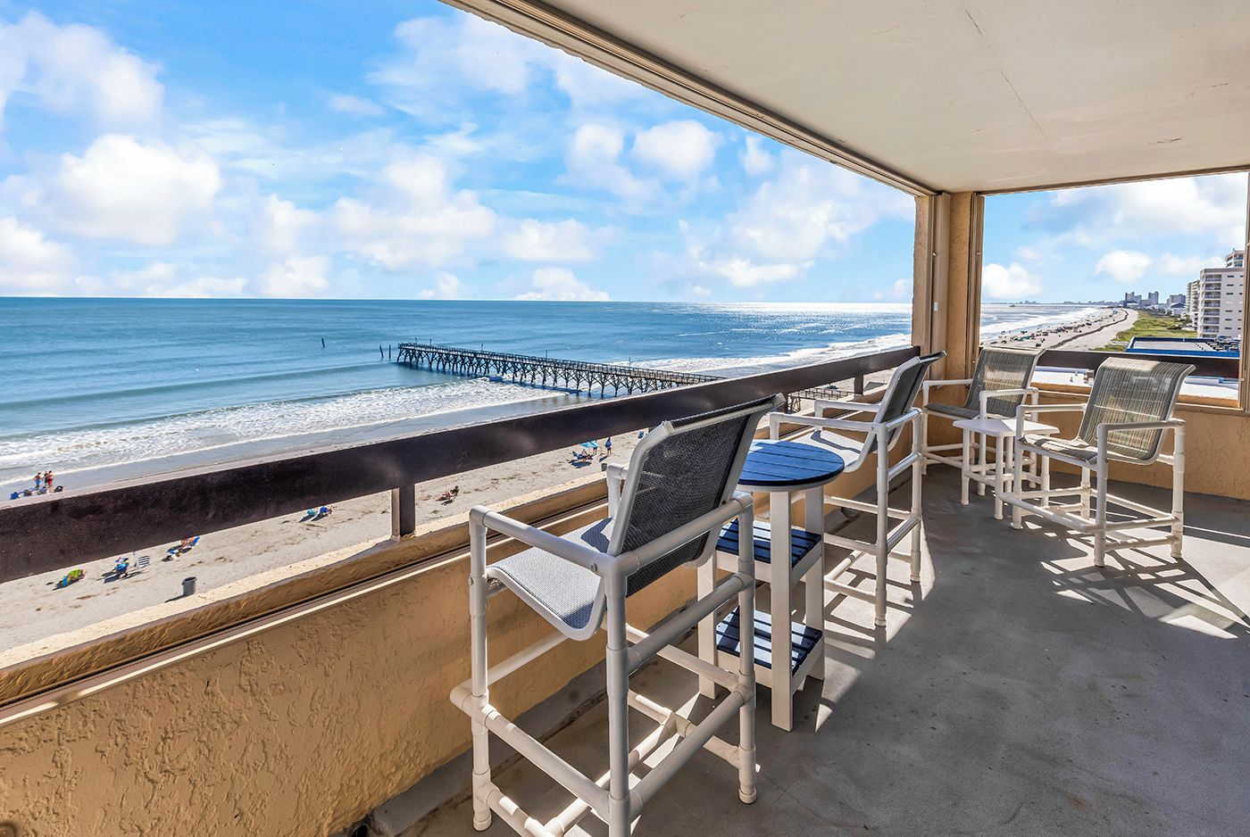 Un balcon avec vue sur la plage et la jetée, doté d’un espace salon extérieur.