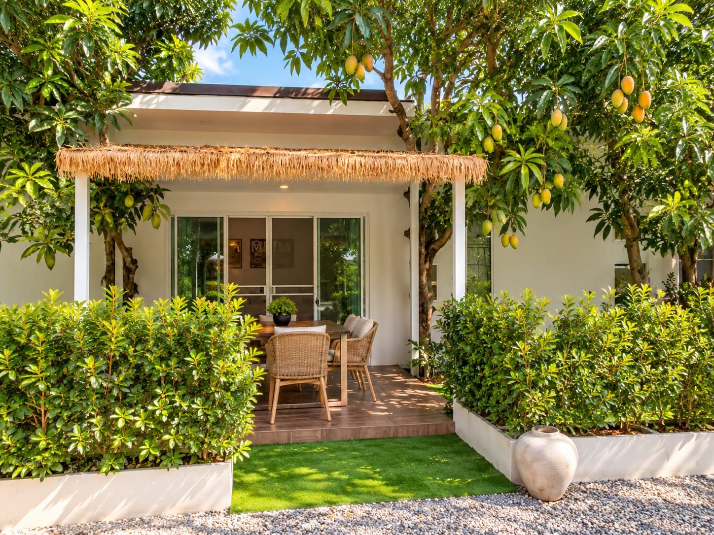 Una casa moderna con un porche cubierto, un comedor con mobiliario de mimbre y un jardín exuberante.