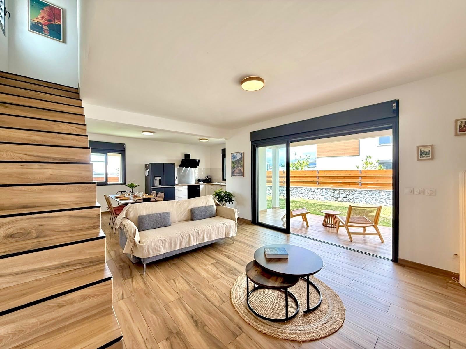A modern living room with a sofa, a coffee table, and a view of a patio with outdoor furniture.