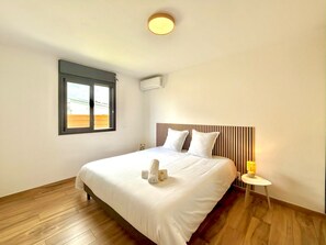 A hotel room with a bed, a bedside table with a lamp, a window with blinds, and an air conditioning unit. - La Villa des Rochers, Calm, Modern and Mountain (Bras-Panon)