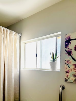 A bathroom with a window, a potted plant, and a shower curtain. - Charming Suite with AC in vibrant Los Angeles (Los Angeles)