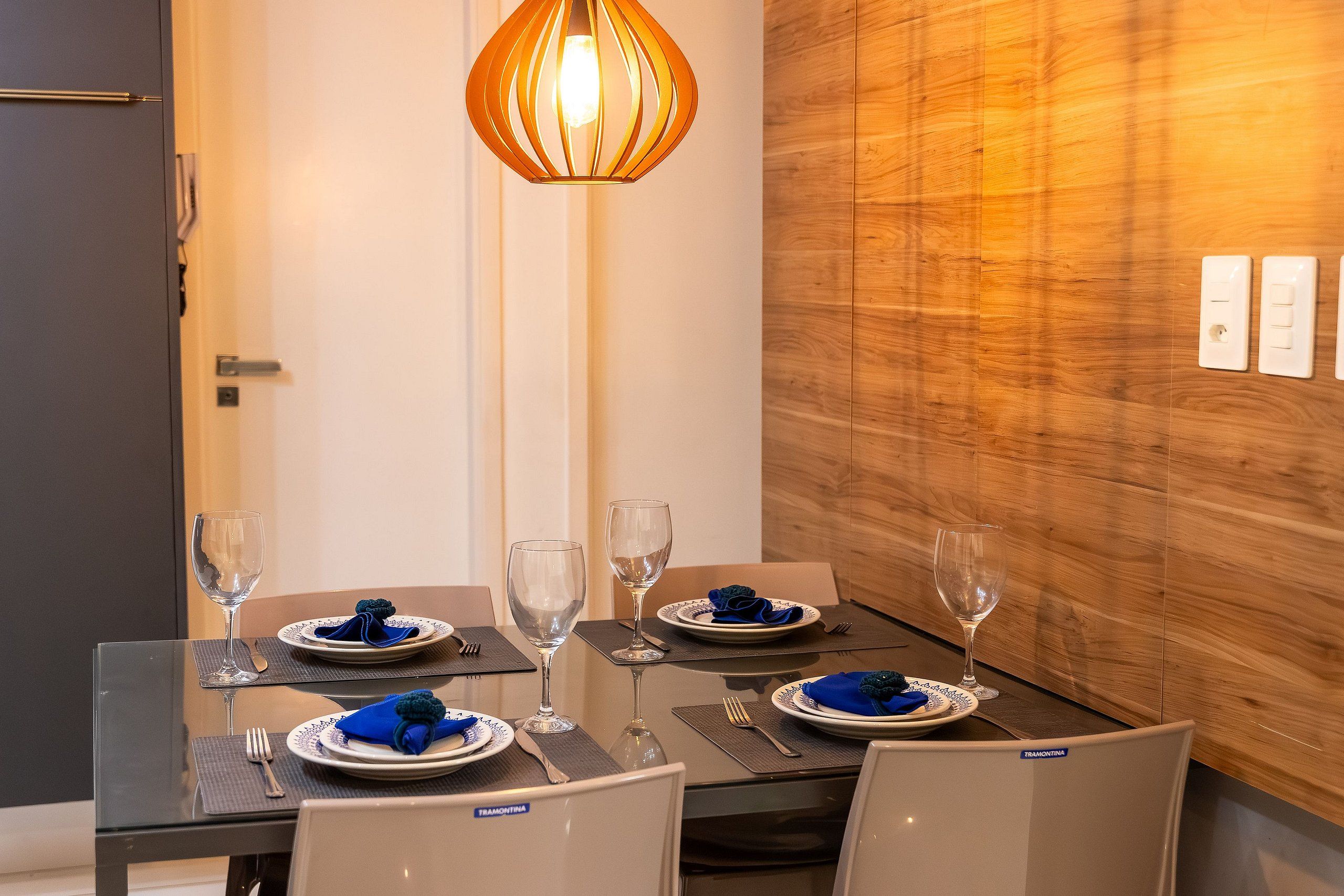 Comedor con mesa lista para cuatro personas, con platos, vasos y cubiertos.
