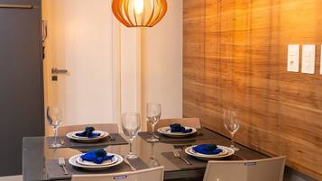 Comedor con mesa lista para cuatro personas, con platos, vasos y cubiertos.