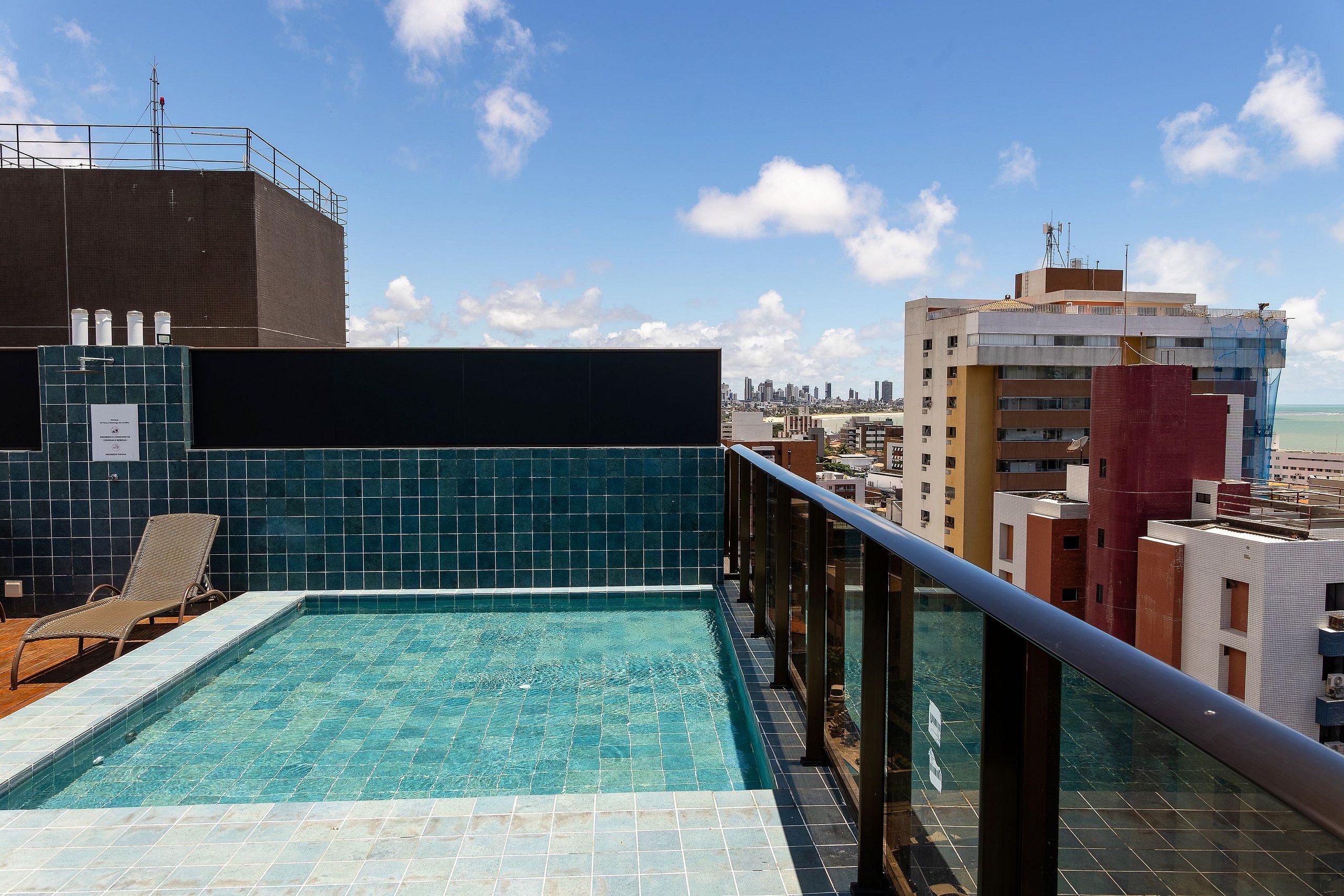 Une piscine sur le toit offrant une vue dégagée sur les gratte-ciel de la ville, un espace couvert avec une rambarde et un fauteuil de relaxation.