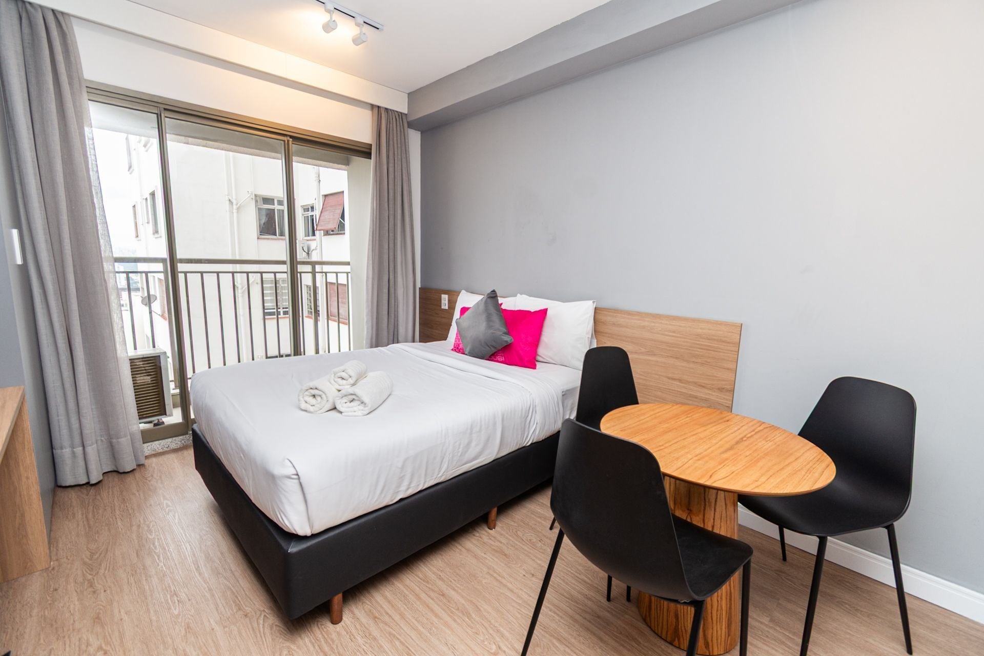 Moderni hotellihuone, jossa on sänky, ruokapöytä ja kaksi tuolia.